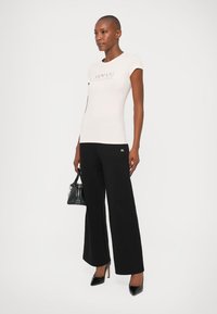 T-shirt branca ajustada com o logótipo "Armani Exchange", combinado com calças largas pretas. Acessorado com uma pequena bolsa preta e saltos altos.