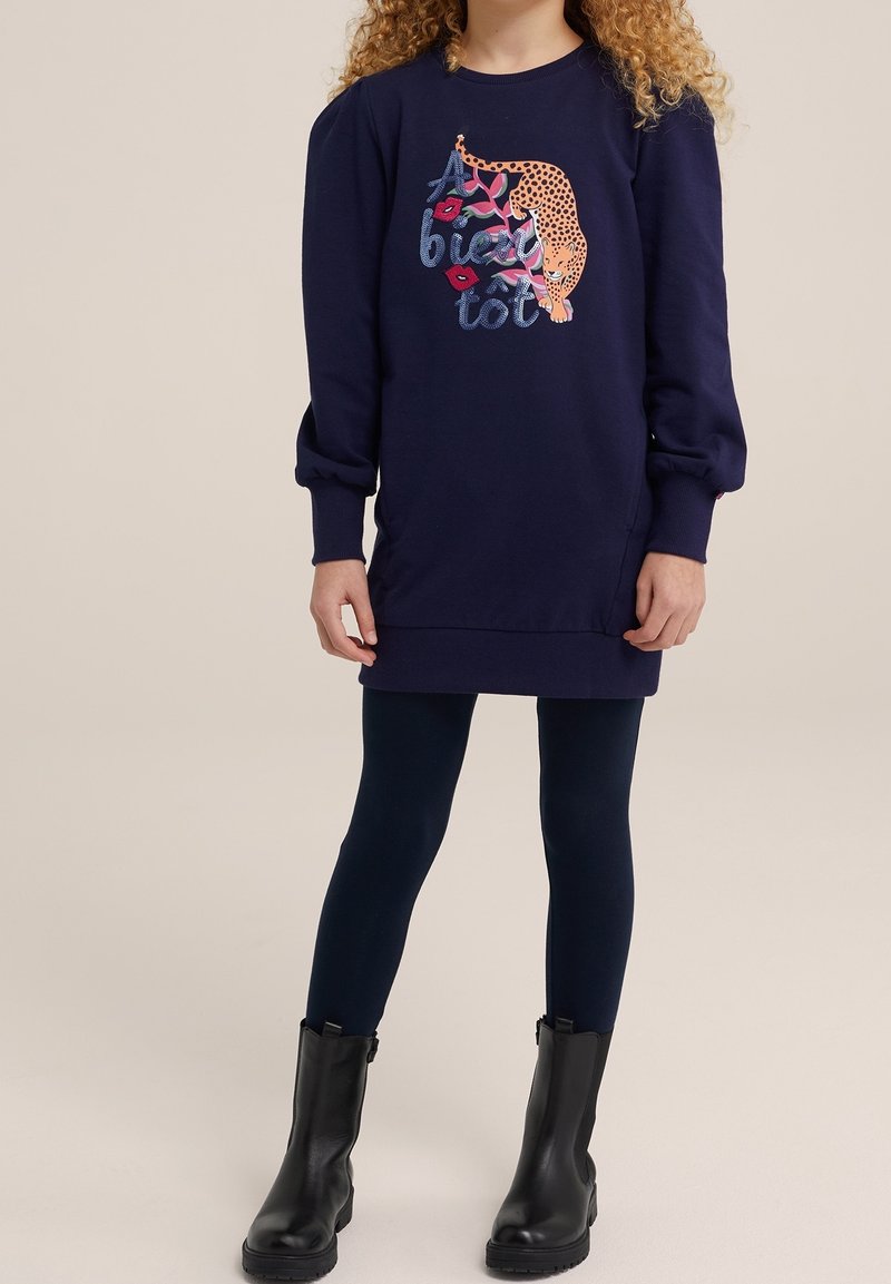 Chica con vestido sudadera azul marino con gráfico de leopardo y texto en francés "À bientôt", mallas azul marino y botines negros.