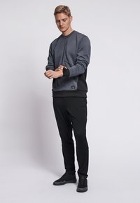 Grå sweatshirt med svarta detaljer, med rund halsringning och ribbade muddar, i kombination med svarta byxor och mörka sneakers. Slät textur.