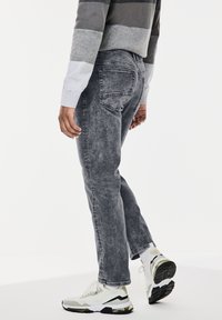 Los jeans gris lavados tienen un corte recto, diseño de cinco bolsillos y un desgaste sutil. Combinados con zapatillas blancas y negras.