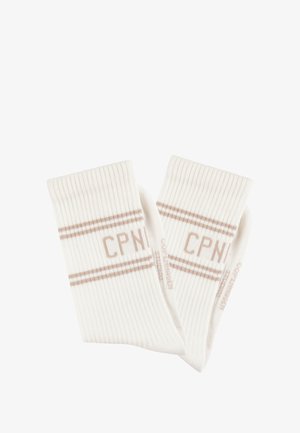 Geribbelde witte sokken met twee beige strepen en de tekst "CPNI". Zachte textuur met een hoogte tot de kuit en gebreid ontwerp.