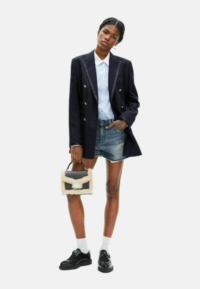 Blazer nero doppiopetto con bottoni dorati, camicia colletto azzurro chiaro, pantaloni shorts in denim scuciti e una piccola borsa nera con dettagli in pelliccia.