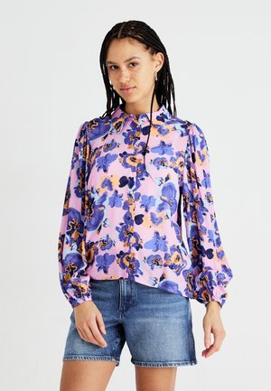 Blomstret bluse med rosa bakgrunn, blå og oransje blomster, lange ermer, knappestolpe foran og lett rynke ved mansjettene.