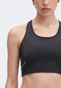 Közeli kép egy személyről, aki fekete sportmelltartót visel racerback kialakítással és apró fényvisszaverő pöttyökkel az oldalon.