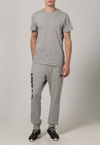 Grå bomullströja med korta ärmar, kombinerad med grå svettbyxor med en svart "NIKE"-logotyp. Svarta sportskor fullbordar outfiten.