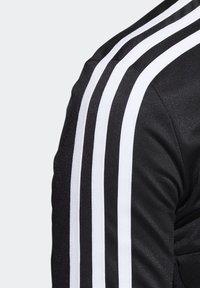 Black sports jacket with white three-stripe design on the sleeves; features textured fabric and a fitted shape.