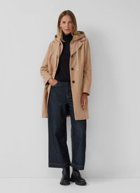 Manteau beige avec une capuche et des cordons de serrage, croisé avec des boutons noirs. Assorti à un jean large noir et des bottes noires. Matière lisse, lignes épurées.