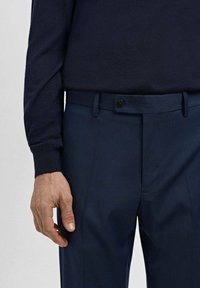 Granatowe spodnie z teksturowanym wzorem, wyposażone w zapięcie na guzik i szlufki na pasek. Połączone z ciemną, dopasowaną koszulą z długim rękawem.