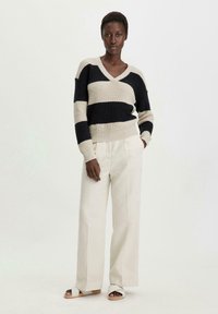 Strickpullover mit V-Ausschnitt in horizontalen navyblauen und beigen Streifen, kombiniert mit hellen, weiten Hosen und einfachen Sandalen.