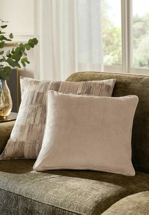 Two decorative pillows, one solid beige and one textured beige with abstract pattern, on an olive-green fabric sofa near a window.
