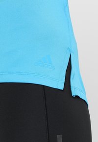 Blue athletic shirt made of smooth material, featuring a side slit design and a small Adidas logo in the bottom left corner.