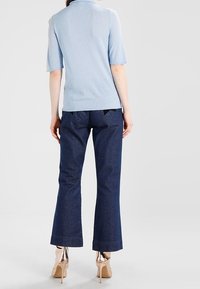 Ljusblå pikétröja med korta ärmar kombinerad med mörka, utsvängda denimbyxor. Outfiten har en figursydd design och minimalistiska detaljer.