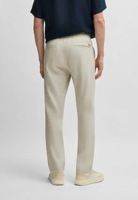 Light beige trousers made of soft fabric, featuring a relaxed fit, elastic waistband, and subtle back pockets. Smooth texture and straight legs.