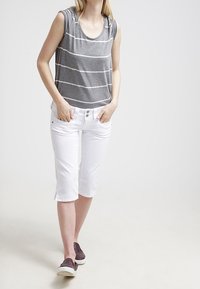 Harmaan raidoilla varustettu hihaton toppi, jossa on pyöreä pääntie, yhdistettynä valkoisiin polvipitkiin housuihin ja vaaleanruskeisiin liu'uttaviin kenkiin.