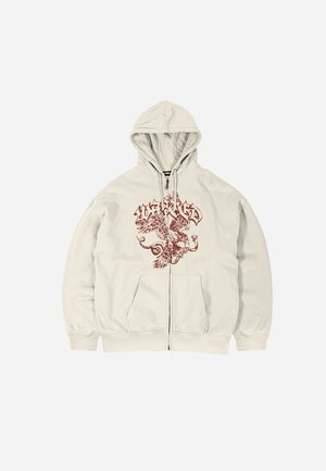 Sweat à capuche couleur beige clair, doté d'une fermeture éclair à l'avant, de deux poches latérales et d'un motif graphique rouge sur la poitrine. Texture douce.