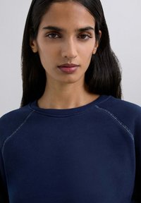 Dunkelblaues Sweatshirt mit geripptem Rundhalsausschnitt, eingesetzten Ärmeln und subtilen Nähdetails. Der Stoff wirkt weich und strukturiert.