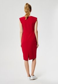Rotes, figurbetontes Kleid mit kurzen Ärmeln, knielangem Design, Rückenschlitz und glattem Stoff. Es zeichnet sich durch eine klare, minimalistische Silhouette aus.