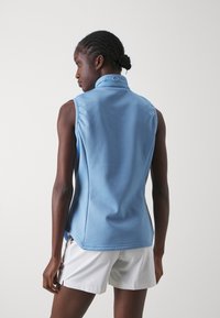 Svijetloplavi bez rukava top s ovratnikom, izrađen od glatkog materijala. Ima diskretni logo na ovratniku i ležeran kroj.