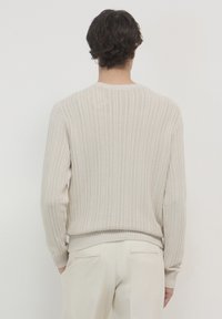Maglione beige lavorato a maglia con coste verticali, dotato di scollatura rotonda e polsini e orlo a coste. Texture liscia, vestibilità comoda.