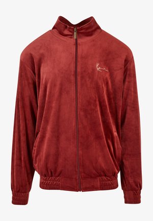 Jachetă zip-up de culoare mahon, fabricată dintr-un material moale și catifelat. Prezintă un guler înalt, manșete elastice și un logo brodat pe piept.