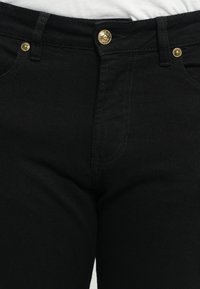 Μαύρα τζιν παντελόνια από τζιν με εφαρμοστή γραμμή, χρυσό κουμπί και ραμμένα σχέδια μπροστά. Λείος υφασμάτινος χαρακτήρας και κλασικό στυλ πέντε τσεπών.