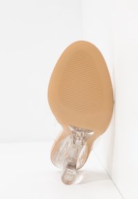 Genomskinlig högklackad sko med en beige sula. Rund tå och genomskinlig ovandel. Trots den tunna klacken är den slät och har en lätt genomskinlighet.