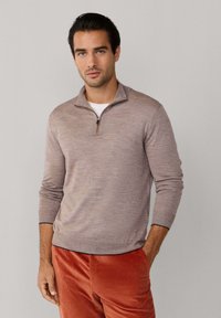  Lichtbruine, gestructureerde trui met een kwart-rits kraag, gedragen over een wit shirt, gecombineerd met oranje corduroy broek.