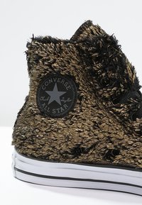 Černé a zlaté vysoké tenisky Converse Chuck Taylor s texturovaným materiálem připomínajícím kožešinu, černou logo nášivkou a bílými gumovými detaily na podešvi.