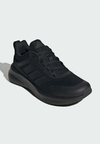 Chaussure de sport noire avec tige en mesh, accents texturés, six œillets et semelle rembourrée pour confort et soutien.