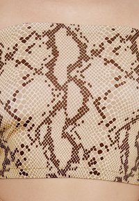 Top sans manches marron et beige présentant un motif de peau de serpent avec des écailles texturées et un design lisse et ajusté.