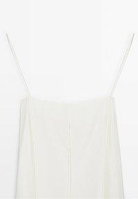 Robe blanche sans manches avec fines bretelles spaghetti et un décolleté droit sur un fond blanc uni.