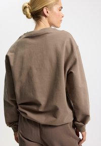 Sudadera de cuello redondo marrón hecha de tela suave, con un corte holgado, hombros caídos y puños acanalados. Diseño liso sin patrones.
