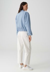 Veste cropped bleu clair avec une taille froncée; assortie à un pantalon blanc à jambe droite et à des baskets blanches. Texture lisse, design décontracté.