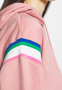 Sudadera rosa con capucha, puños acanalados y rayas horizontales en azul, verde, blanco y rosa en las mangas. Textura suave.