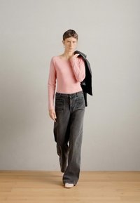 Ružový top s dlhým rukávom, šedé široké džínsy, model nesúci čiernu koženú bundu. Jednoduchý dizajn, hladká textura, neutrálne farby.