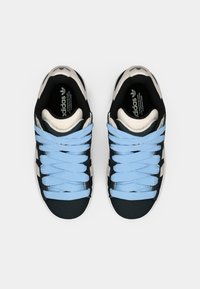 Black and cream sneakers with blue laces, featuring a textured upper and a round toe. Logo visible on the insole.