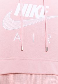 Ljusrosa hoodie med vit Nike-logotyp och texten "AIR". Har en mjuk tygkvalitet och silverfärgade snörtoppar, med en meshdetalj i nederkant.