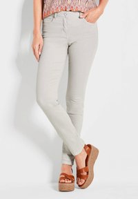 Hellgraue Skinny-Jeans aus einem glatten Stoff, kombiniert mit braunen Sandalen mit Keilabsatz, die eine geflochtene Jutebasis und einen flachen Absatz haben.