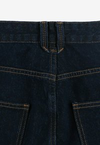 Ciemnoniebieskie dżinsy z pasem, kontrastowym pomarańczowym szwem, dwiema tylnymi kieszeniami i gładką fakturą.