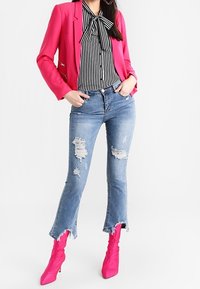 En ljusrosa blazer över en svart och vit randig blus, i kombination med slitna blå jeans och rosa ankelstövlar med en samlad textur.