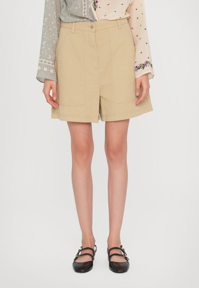 Shorts en coton khaki avec une coupe décontractée, présentant deux poches avant et un devant plat. Associés à des chaussures noires à lanières faciles à enfiler.