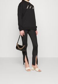 Black sweatshirt with three white logo prints, fitted black leggings with side slits, cream open-toe block-heel sandals, and a black chain-accented bag.