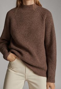 Maglione a coste marrone con collo alto, maniche raglan e vestibilità comoda, abbinato a pantaloni chiari.