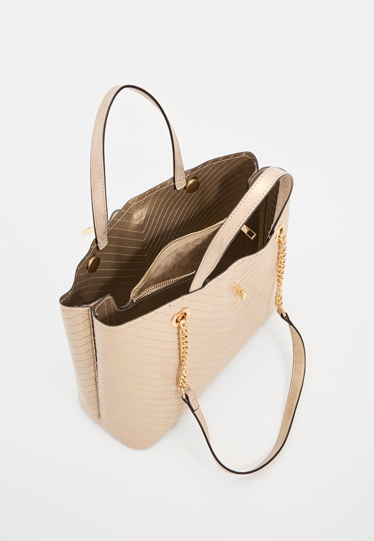 Bolsa tote beige con textura de acolchado, dos asas resistentes y un acento de cadena dorada. El interior cuenta con un bolsillo con cremallera y dos secciones abiertas.