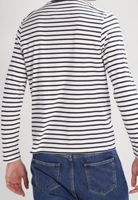 Langarm gestreiftes Hemd in Weiß und Marineblau, mit Rundhalsausschnitt und lockerer Passform, kombiniert mit blauen Jeans mit Gesäßtaschen.