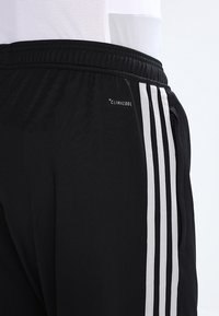 Černé sportovní kalhoty s bílými trojitými bočními proužky, elastickým pasem, kapsou na zip a brandingem "Climacool" na boku.