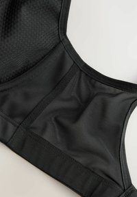 Zwarte sportbeha met een mix van gladde en textuur geperforeerde panelen, een brede elastische band en versterkte naden voor ondersteuning en flexibiliteit.