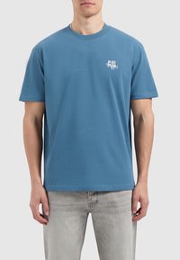 Blauwe katoenen t-shirt met korte mouwen en ronde hals. Heeft een witte tekstprint op de linkerkant van de borst. Zachte textuur, casual pasvorm.