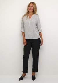 Chemise rayée à manches longues blanche et noire, avec un col rond et des manches retroussées, associée à un pantalon noir slim-fit et des escarpins noirs pointus.