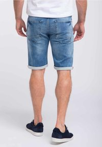 Modré džínové šortky s ohrnutými okraji, pěti kapsami a vymyšleným vzhledem. Nosí se s námořnickými teniskami, což ukazuje na uvolněný styl.